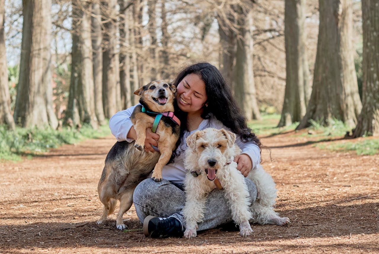 A joyful woman with two dogs sitting in a sunlit Montevideo park path.